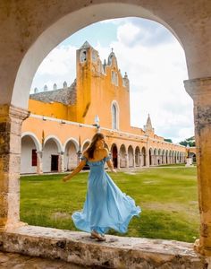 a woman in a blue dress is walking through an archway to a building with arches