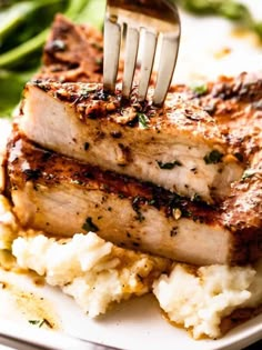 a fork sticking out of some meat on top of mashed potatoes