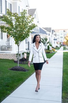 a woman is walking down the sidewalk in front of some white houses and green grass