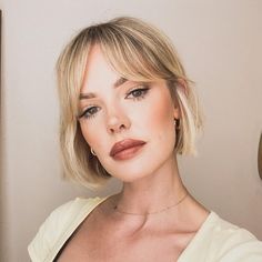 a woman with short blonde hair wearing a white shirt and gold hoop earrings is looking at the camera