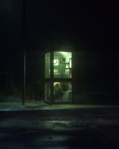 a person is sitting in a bus stop at night with their head inside the phone booth