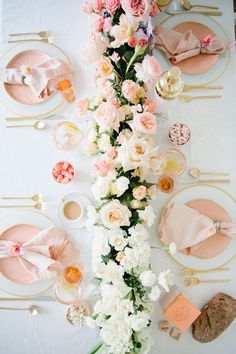 the table is set with pink and white flowers, gold place settings, and napkins