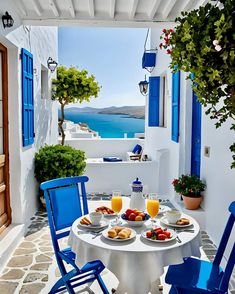 an outdoor table with plates of food and drinks on it next to blue shutters