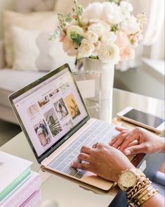 a woman is typing on her laptop while sitting at a table with flowers in the background