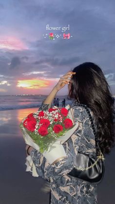 a woman is holding flowers and looking at the sunset on the beach with her back to the camera