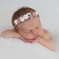 a baby wearing a flower headband laying on top of a white surface with her hands under her face