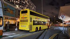 a yellow double decker bus is parked on the side of the road at night time