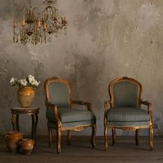 two chairs sitting next to each other in front of a wall with chandelier