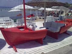 a red boat sitting on top of a wooden pier next to chairs and umbrellas