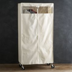 a white garment rack on wheels with clothes hanging in the top and bottom section, against a black wall