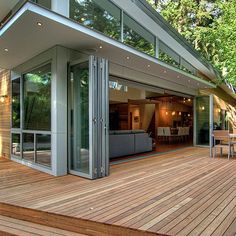 a wooden deck with chairs and tables next to a house in the woods on stilts