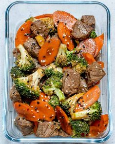 a glass dish filled with broccoli, carrots and beef covered in sesame seeds