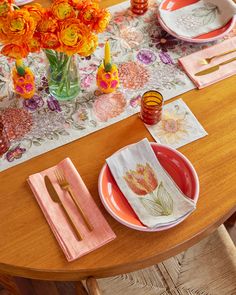 a wooden table topped with plates and napkins next to a vase filled with flowers