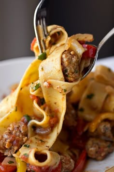 a fork full of pasta with meat, peppers and sauce being lifted from the plate