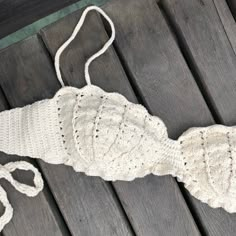 a white crocheted bikinisuit laying on top of a wooden bench next to a string