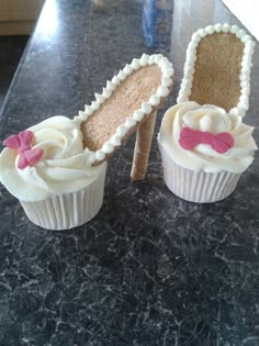 two cupcakes with white frosting and pink bows on them sitting on a counter