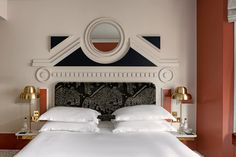 a bed with white sheets and pillows next to a mirror on the wall above it