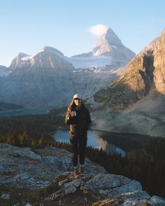 a woman standing on top of a mountain next to a lake with mountains in the background