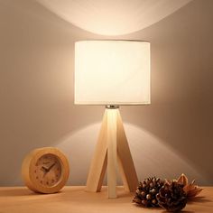 a wooden table lamp with a white shade on it and a pine cone next to it