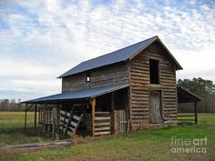 an old wooden barn in the middle of a field with a metal roof on it