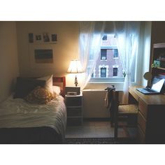 a small bedroom with a bed, desk and lamp in front of a large window