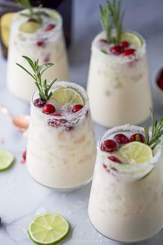 three glasses filled with drinks and garnished with cranberries, limes and rosemary