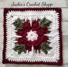 a red and white crocheted square with green leaves on the center is shown