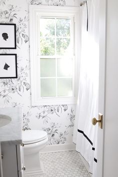 a white toilet sitting next to a window in a bathroom with black and white wallpaper