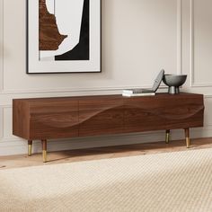 a modern wooden sideboard in the corner of a room with a painting on the wall