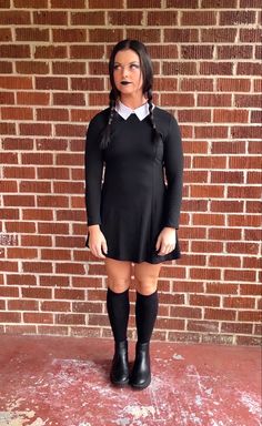 a woman in black dress and suspenders standing next to a brick wall with her mouth open