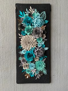 an art piece made out of paper flowers on a black board with silver and blue accents