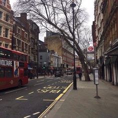 a red double decker bus driving down a street next to tall buildings