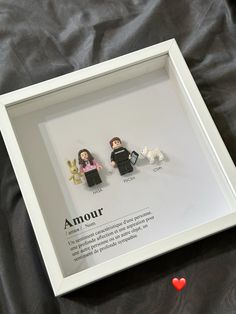 two legos are in a white frame on a black sheet with a red heart