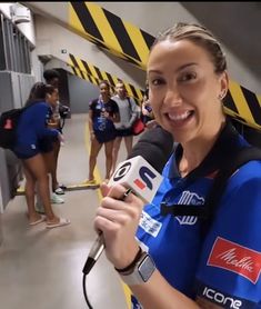 a woman is holding a microphone and wearing a blue shirt while talking to the camera