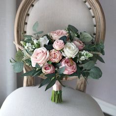 a bouquet of pink and white flowers sitting on top of a chair with greenery