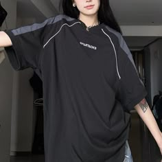 a woman with long black hair and piercings wearing a black t - shirt standing in front of a mirror