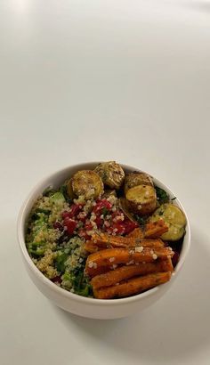 a bowl filled with carrots, broccoli and other vegetables on top of a white table