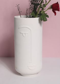 a white vase with flowers in it sitting on a table next to a pink wall