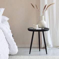 a white vase sitting on top of a small table next to a bed with pillows