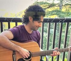 a man playing an acoustic guitar on a balcony