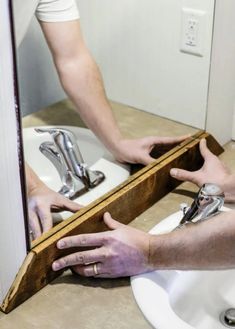 a man is doing something with his hands in the bathroom sink while holding onto an unfinished piece of wood