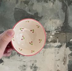 a hand holding a small bowl with green designs on the bottom and pink rim, in front of a grungy wall