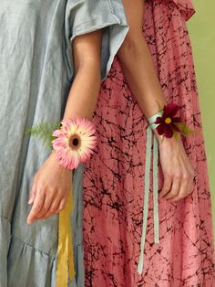 two women wearing matching bracelets with flowers on their wristlets, one holding a flower