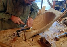 a man working on a wooden boat in a shop with other woodworking tools around him