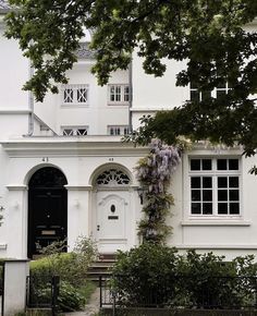 a white house with lots of windows and plants growing on the side of it's front door