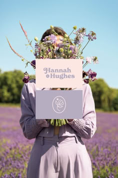 a woman standing in a lavender field holding a sign with the words hannah & hughes on it