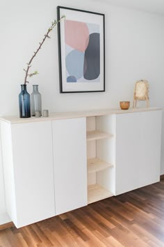 a white cabinet with shelves and vases on top of it in a living room