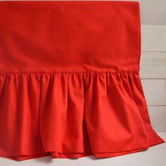 a red bed skirt with ruffles on the bottom and side, sitting on a white wooden floor