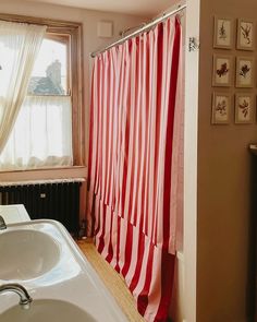 a red and white shower curtain next to a bathtub with a sink in front of it