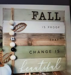 a wooden sign that says fall is proof that change is beautiful with white pumpkins and greenery